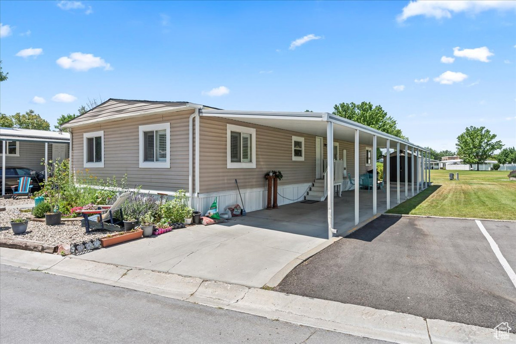 Manufactured / mobile home featuring asphalt driveway, a front yard, and an attached carport