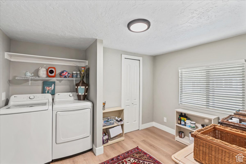 Washroom featuring washer and dryer, light wood-style floors, and a textured ceiling
