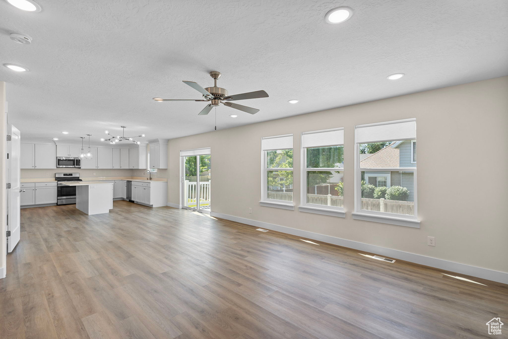 Unfurnished living room with a ceiling fan, light wood-type flooring, recessed lighting, a textured ceiling, and a chandelier