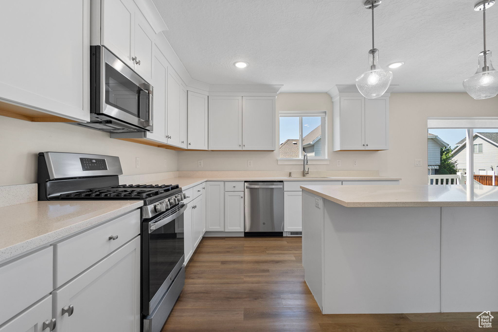 Kitchen with stainless steel appliances, light countertops, white cabinets, dark wood-type flooring, and recessed lighting