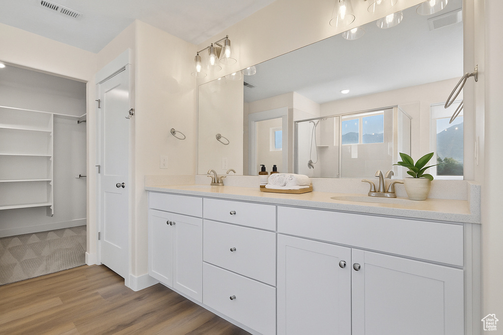 Full bathroom featuring double vanity, a shower stall, wood finished floors, and a spacious closet