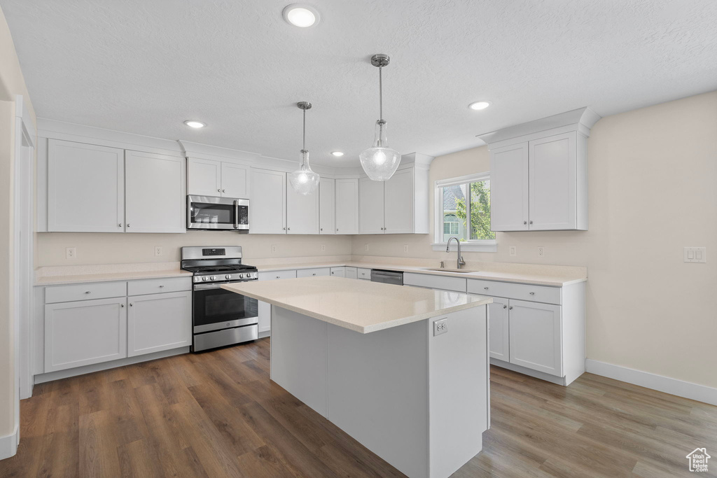 Kitchen with appliances with stainless steel finishes, white cabinets, light countertops, wood finished floors, and a center island