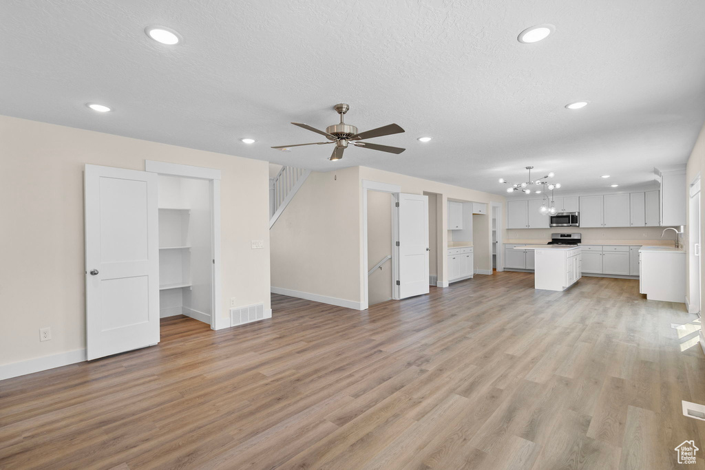Unfurnished living room featuring recessed lighting, a chandelier, ceiling fan, light wood finished floors, and stairs