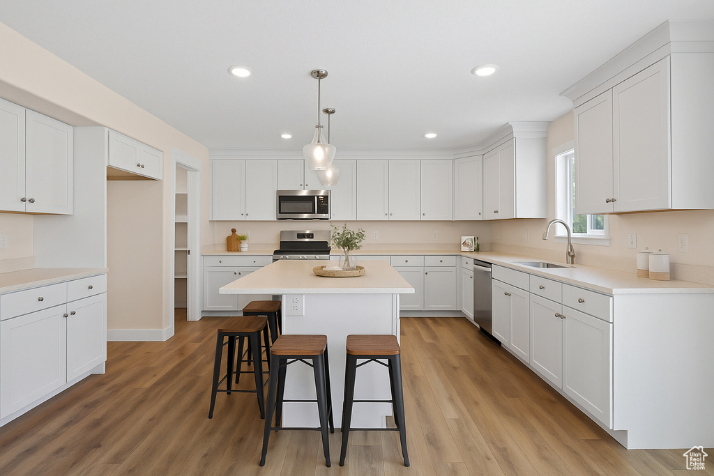 Kitchen with stainless steel appliances, a kitchen bar, a center island, white cabinets, and light wood-style floors