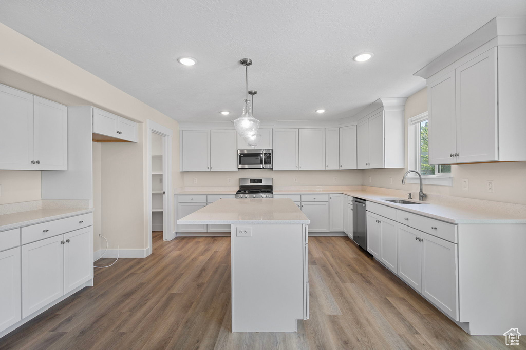Kitchen with stainless steel appliances, white cabinetry, a center island, wood finished floors, and recessed lighting