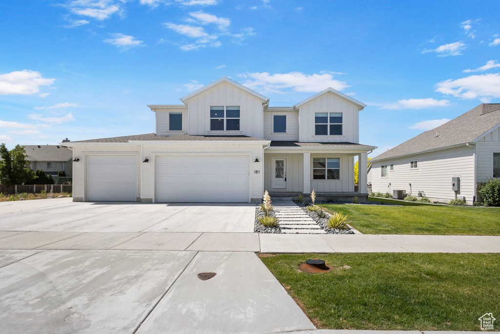 Modern farmhouse featuring board and batten siding, driveway, a front lawn, and an attached garage
