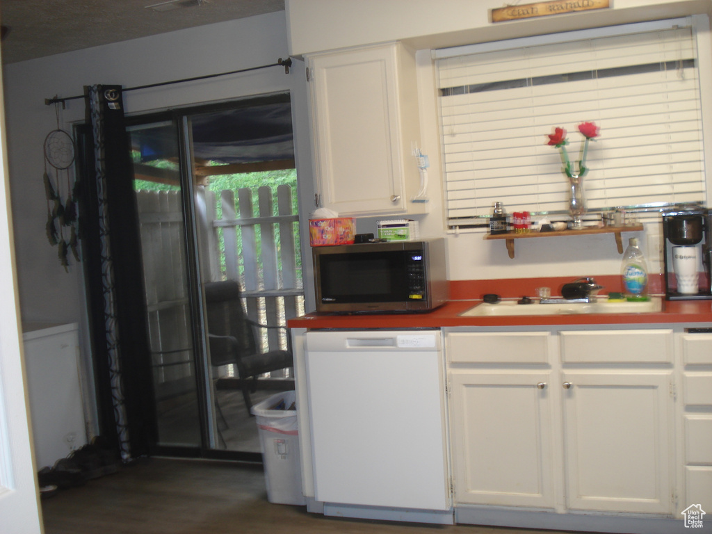 Kitchen with stainless steel microwave, white dishwasher, white cabinets, and dark wood-style floors