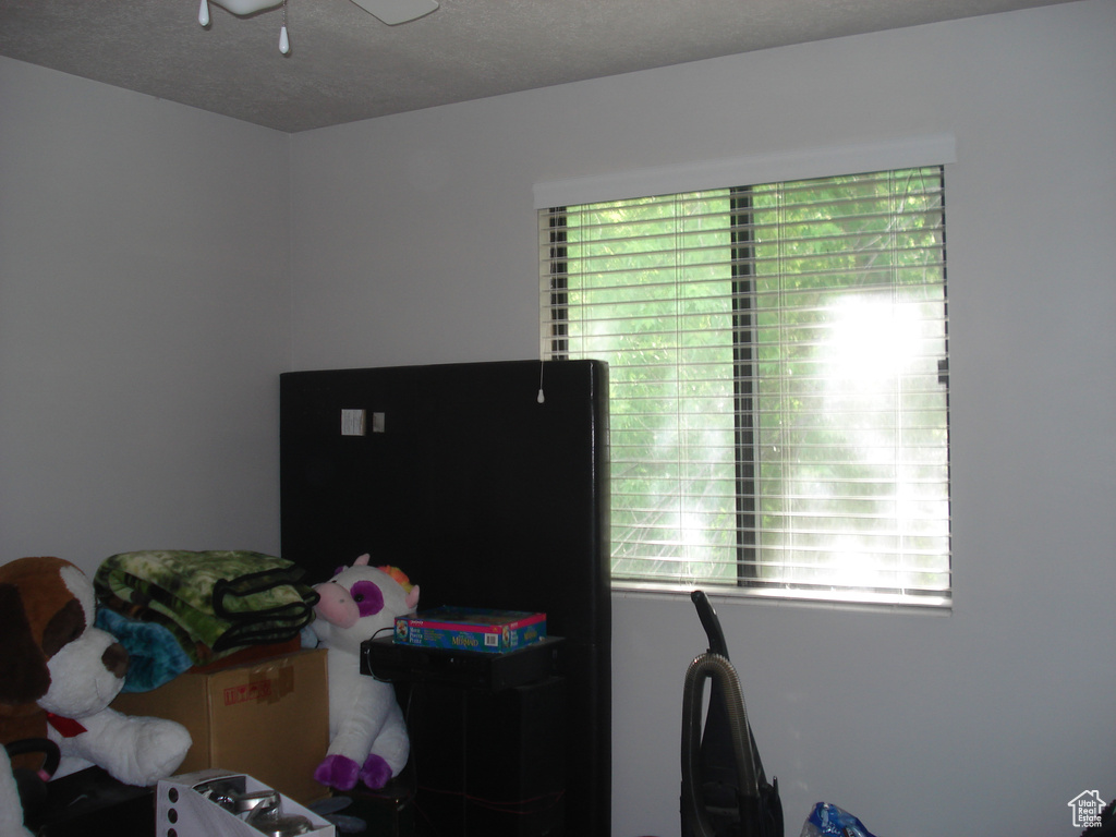 Bedroom with multiple windows, a textured ceiling, and freestanding refrigerator