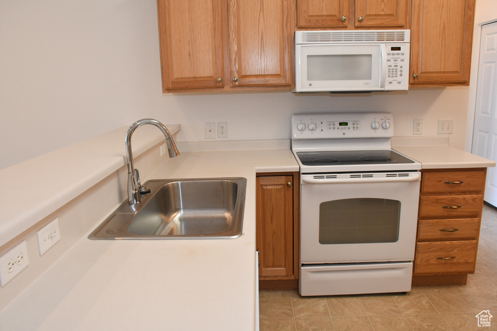 Kitchen with white appliances, a sink, light countertops, light tile patterned floors, and brown cabinets