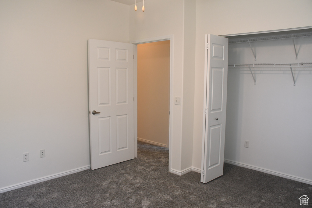 Unfurnished bedroom with dark colored carpet, a closet, and baseboards