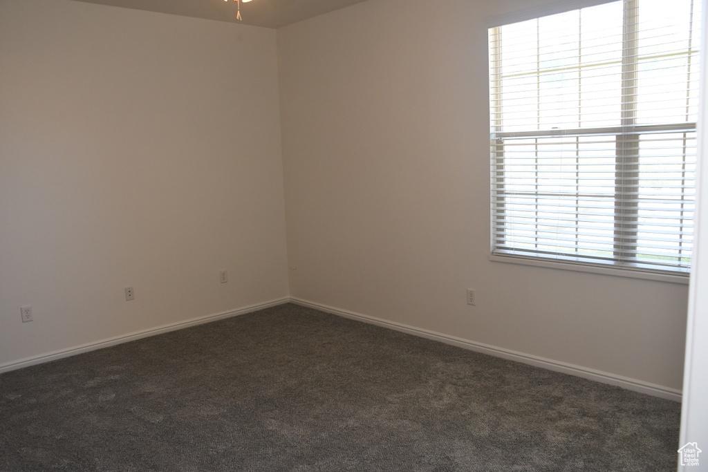 Empty room with dark colored carpet, baseboards, and ceiling fan