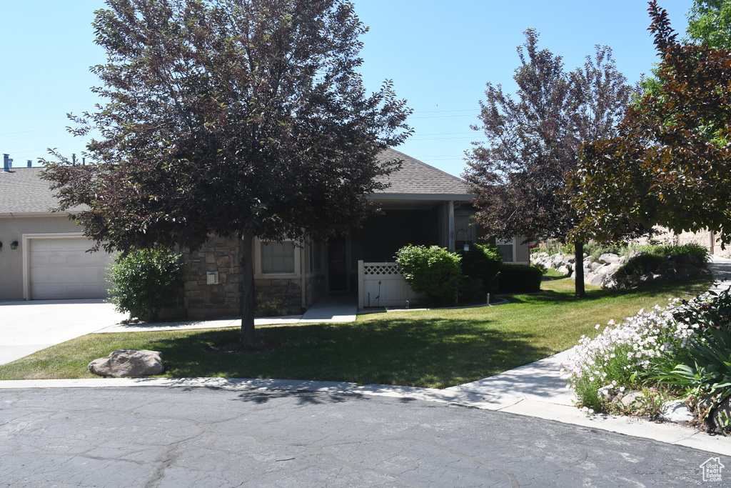 View of property hidden behind natural elements with a garage, a front lawn, roof with shingles, and concrete driveway