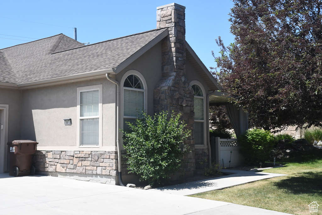 View of side of property featuring stone siding, stucco siding, roof with shingles, a chimney, and a lawn