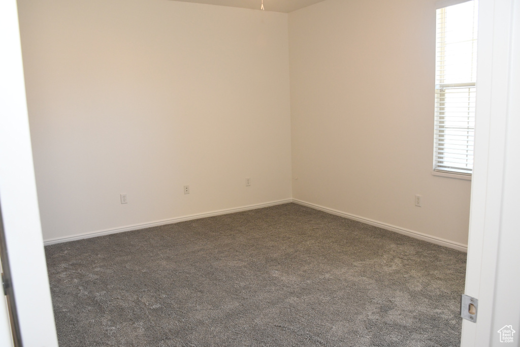 Unfurnished room featuring dark colored carpet and baseboards