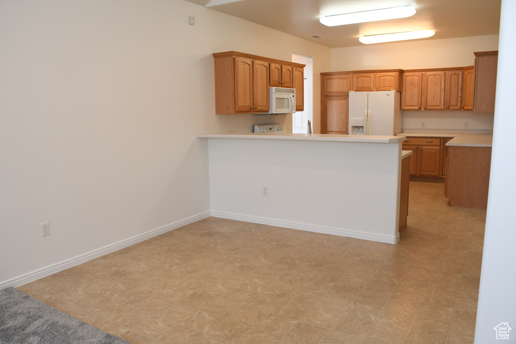 Kitchen featuring white appliances, light countertops, a peninsula, light flooring, and brown cabinets