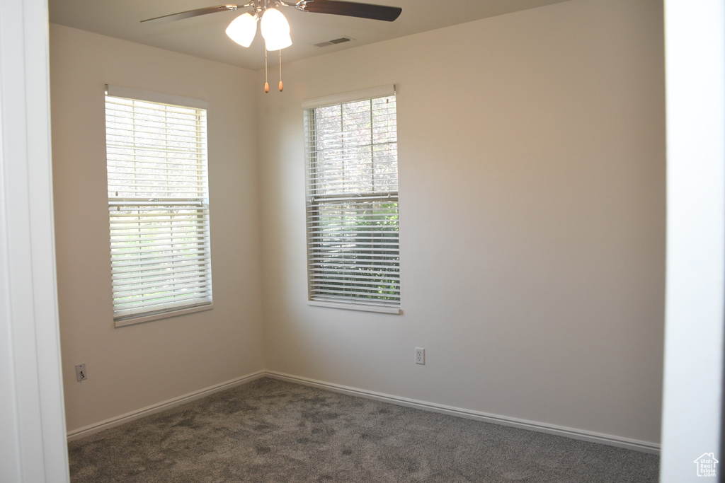 Empty room featuring a ceiling fan, dark colored carpet, and baseboards