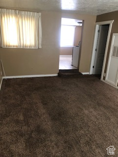 Empty room with dark carpet and a textured ceiling