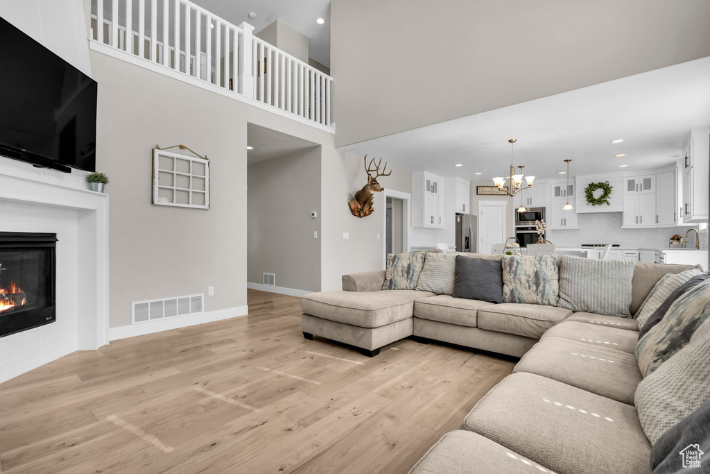 Living room featuring a chandelier, light wood finished floors, a glass covered fireplace, recessed lighting, and a high ceiling