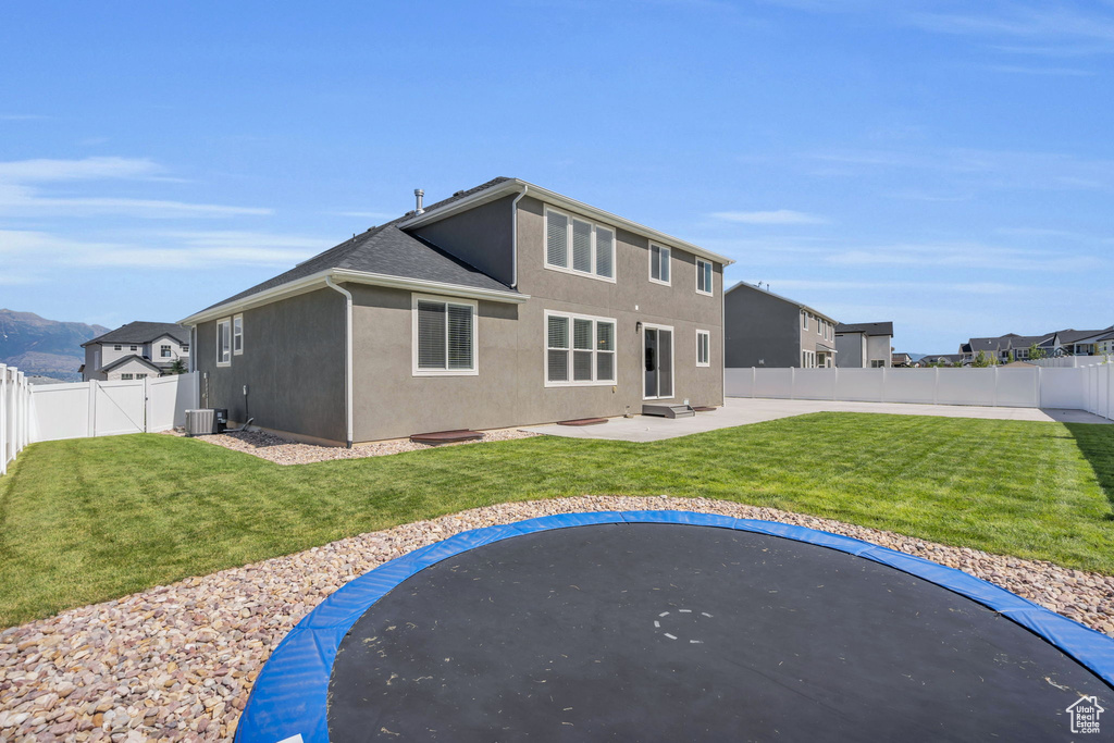 Rear view of property with a trampoline, a fenced backyard, stucco siding, and a patio area