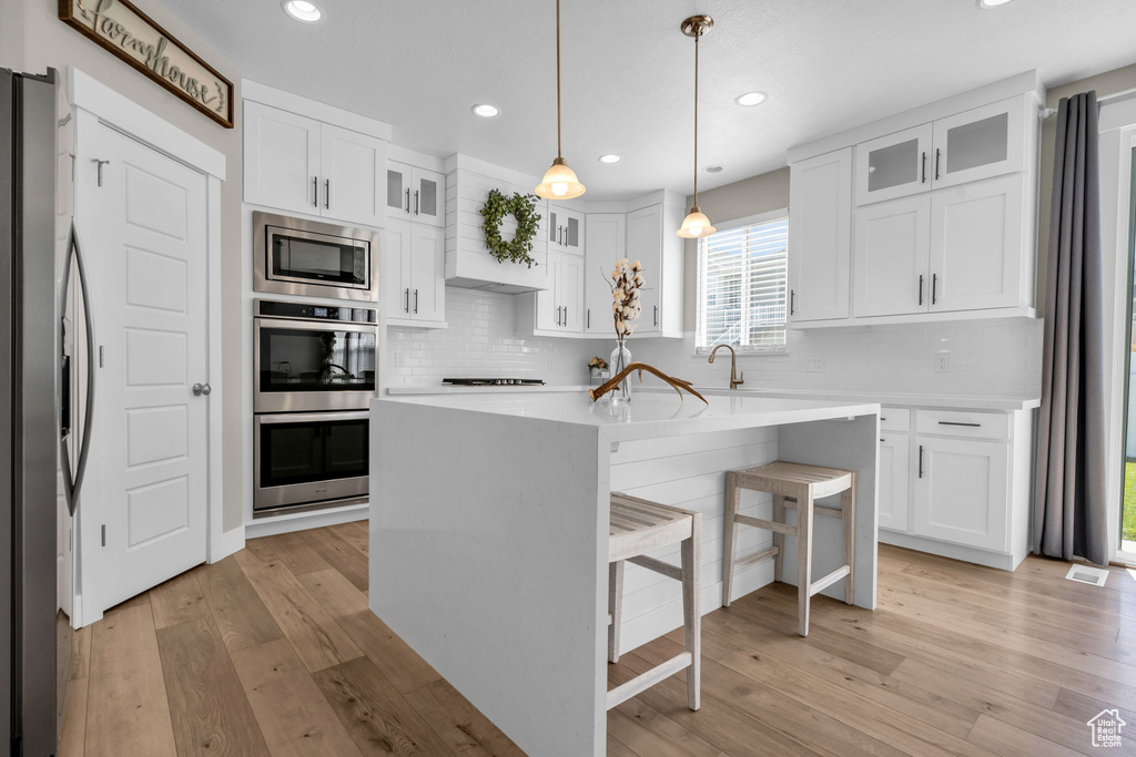Kitchen featuring stainless steel appliances, tasteful backsplash, white cabinetry, light wood finished floors, and light countertops