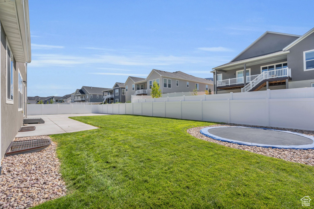 Fenced backyard with a trampoline, a residential view, and a patio area