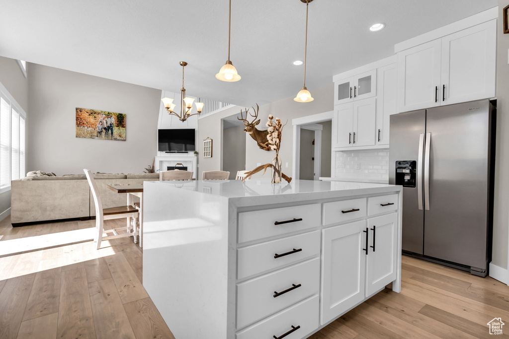 Kitchen featuring stainless steel fridge, open floor plan, light wood-type flooring, glass insert cabinets, and white cabinets