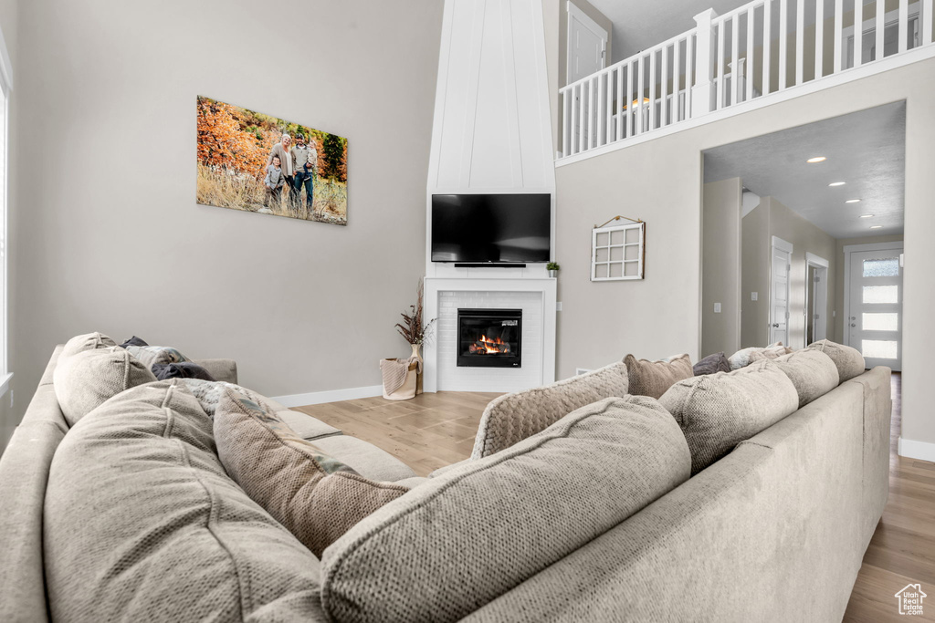 Living area with wood finished floors, a towering ceiling, a glass covered fireplace, and recessed lighting