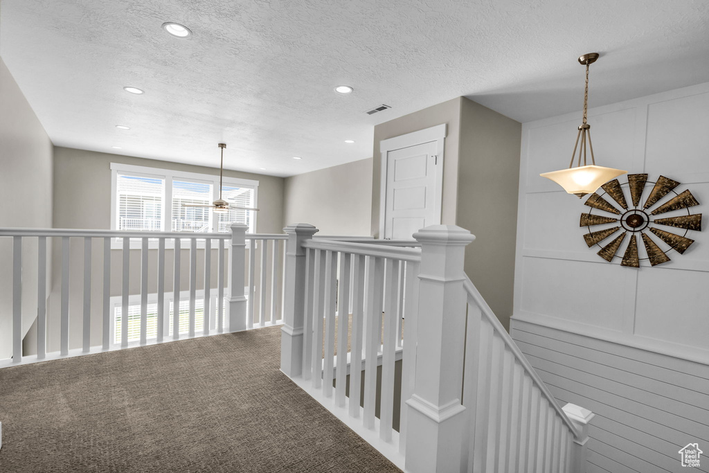 Corridor featuring an upstairs landing, a decorative wall, recessed lighting, a textured ceiling, and carpet