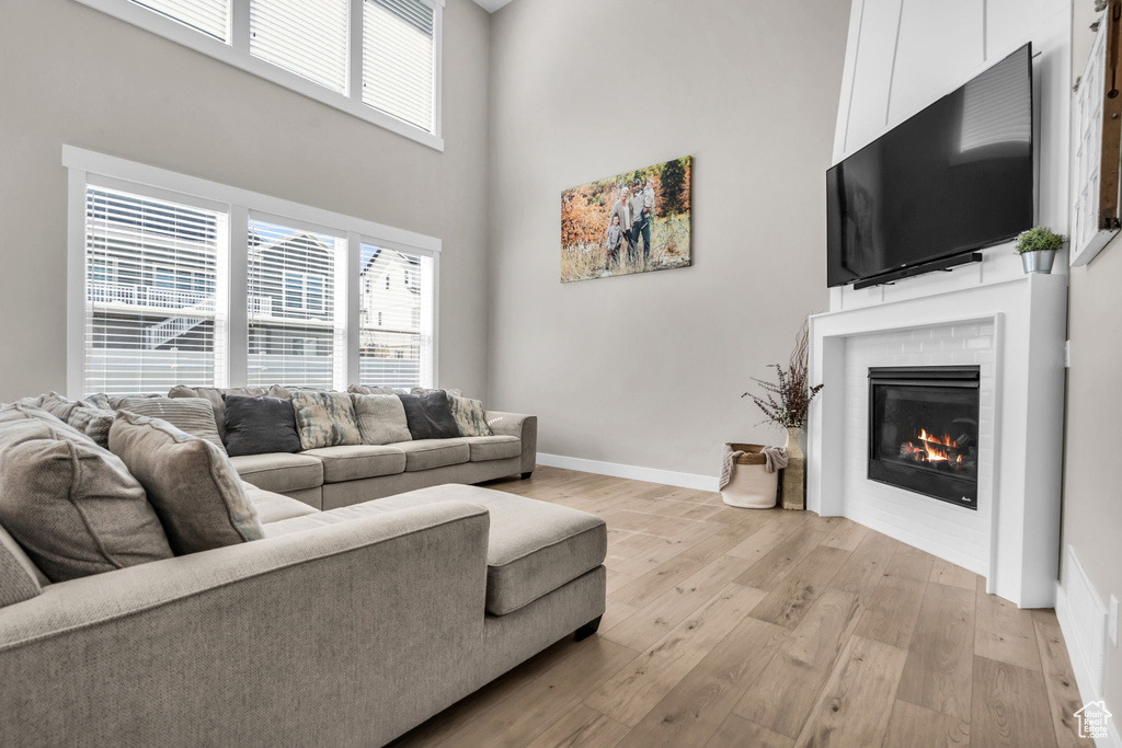 Living room featuring a towering ceiling, light wood-type flooring, a fireplace, and healthy amount of natural light