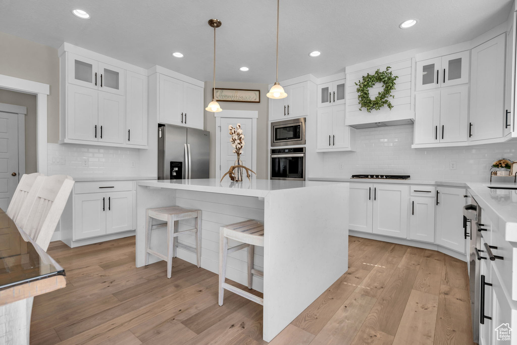 Kitchen with appliances with stainless steel finishes, a breakfast bar, light wood-style flooring, decorative backsplash, and recessed lighting