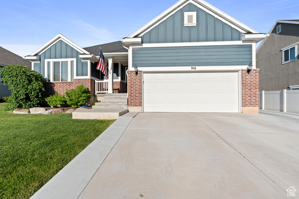 View of front facade featuring board and batten siding, driveway, a front yard, a garage, and brick siding