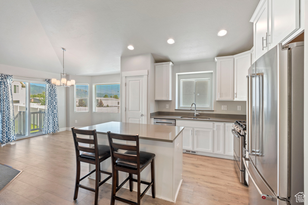 Kitchen with stainless steel appliances, a chandelier, light wood-style floors, white cabinets, and recessed lighting