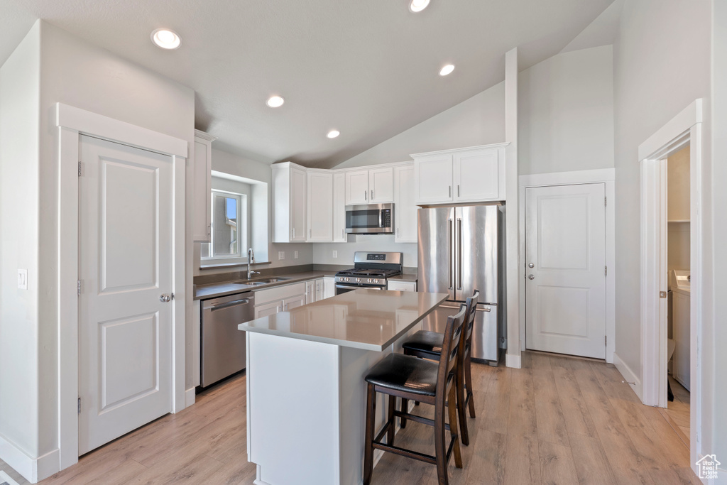 Kitchen featuring appliances with stainless steel finishes, vaulted ceiling, white cabinetry, a center island, and light wood-type flooring