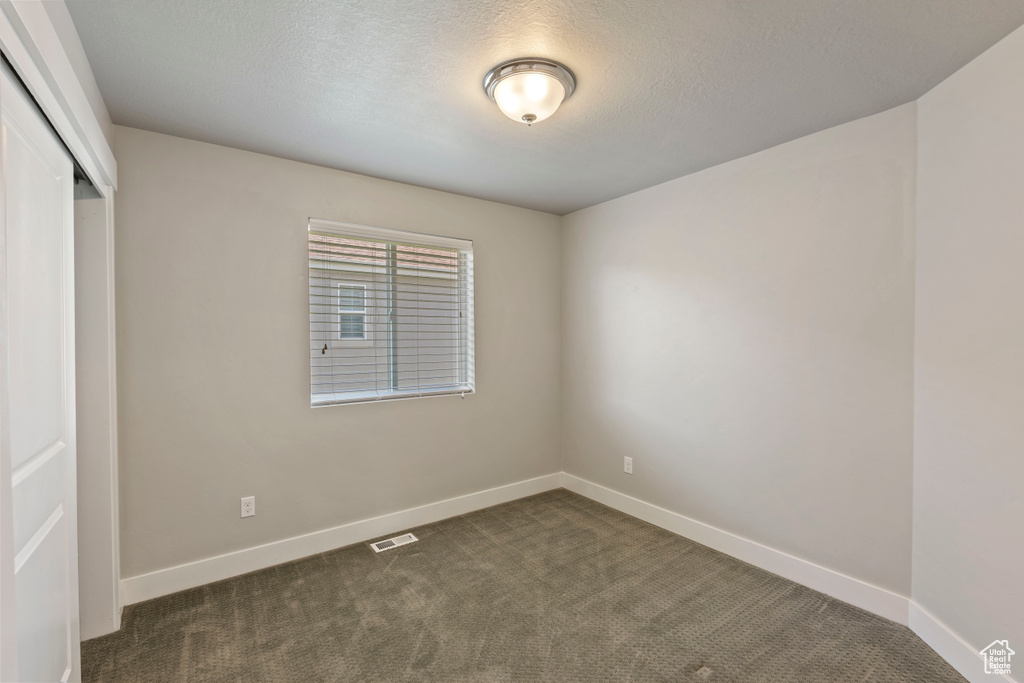 Unfurnished bedroom with a closet, dark colored carpet, and a textured ceiling