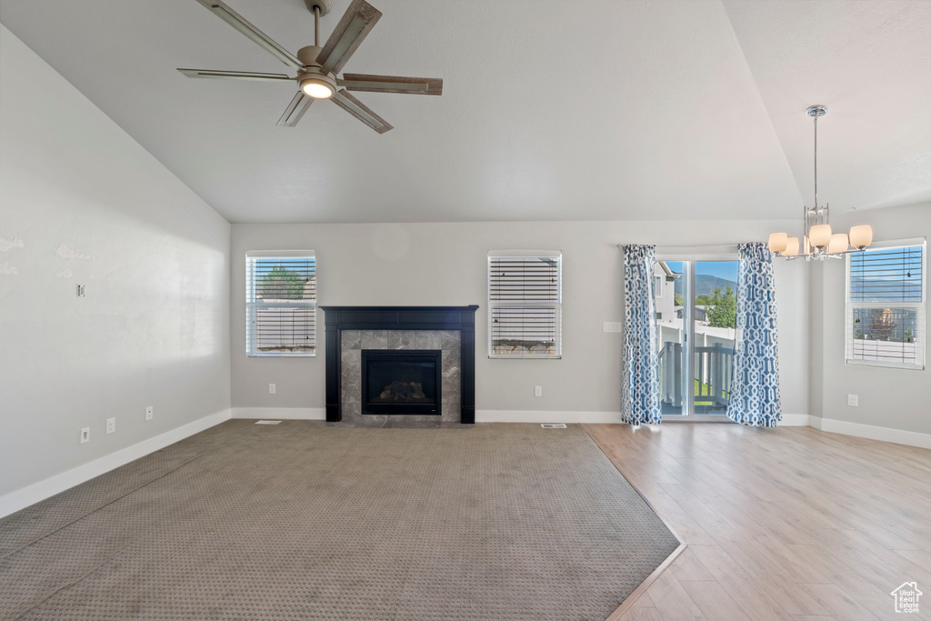 Unfurnished living room featuring a chandelier, plenty of natural light, a ceiling fan, a tile fireplace, and high vaulted ceiling
