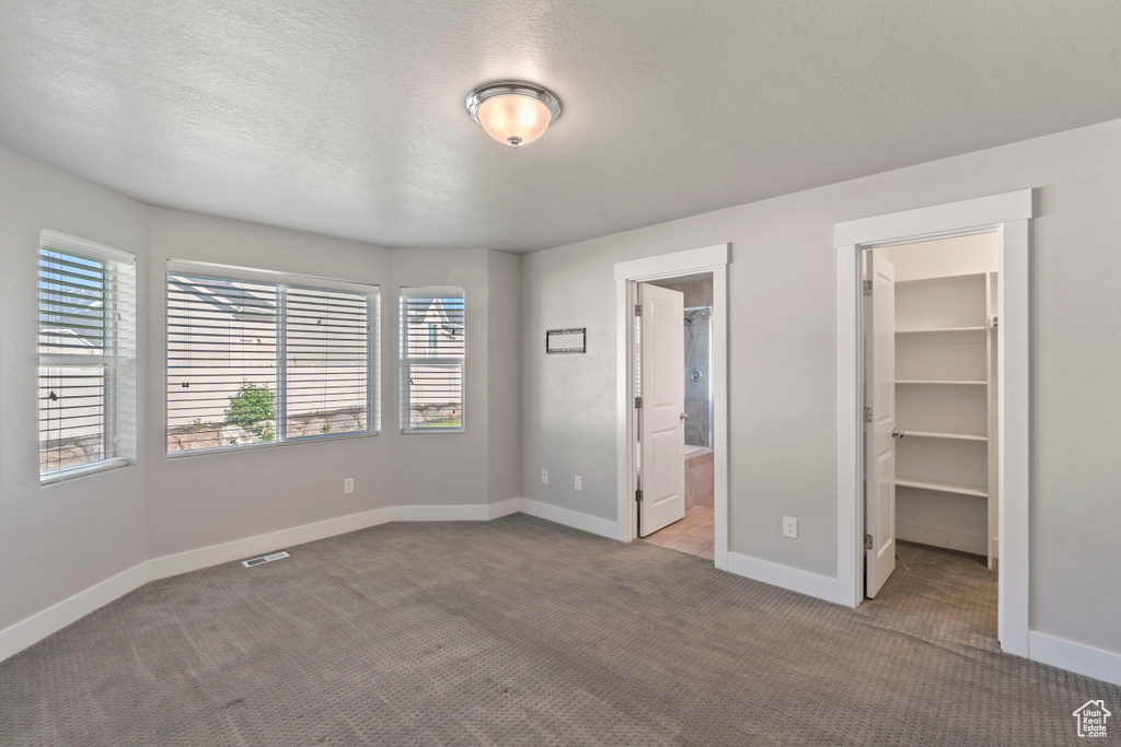 Unfurnished bedroom with a spacious closet, carpet flooring, a closet, ensuite bath, and a textured ceiling
