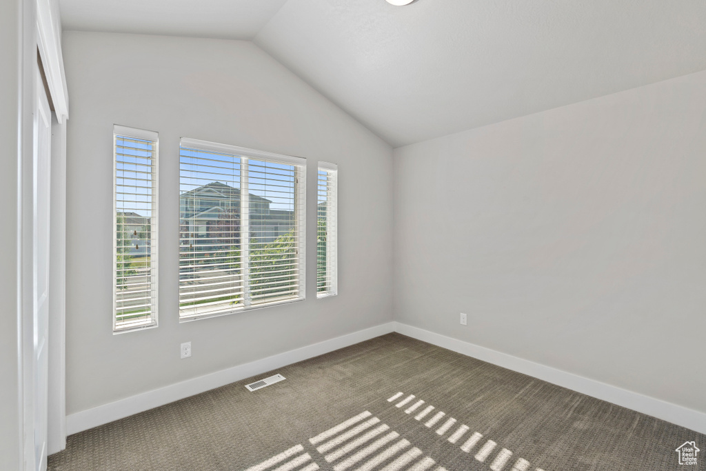 Unfurnished room with lofted ceiling and dark colored carpet