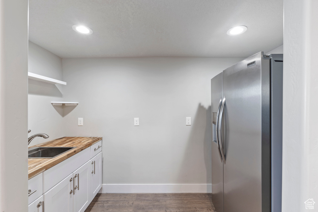 Kitchen featuring stainless steel fridge, open shelves, wood counters, white cabinetry, and dark wood-style flooring