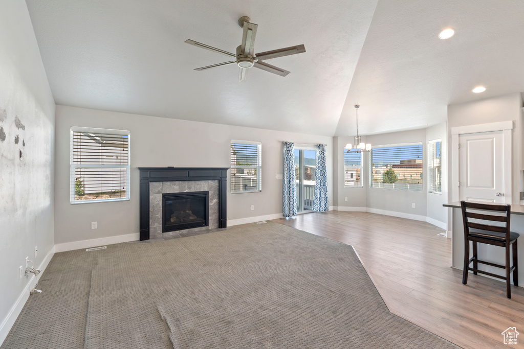 Unfurnished living room featuring a chandelier, a tiled fireplace, ceiling fan, wood finished floors, and vaulted ceiling