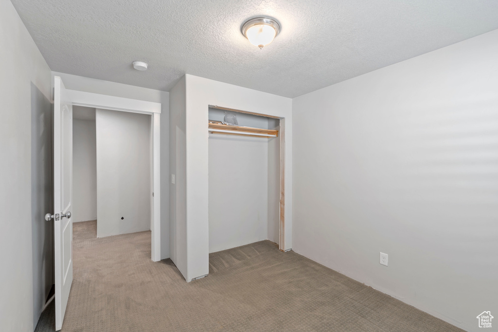 Unfurnished bedroom with light colored carpet, a closet, and a textured ceiling
