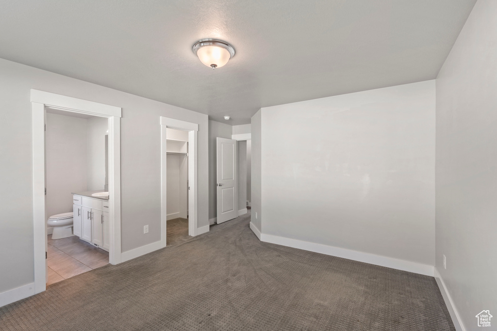 Unfurnished bedroom featuring a walk in closet, light colored carpet, ensuite bath, and a closet