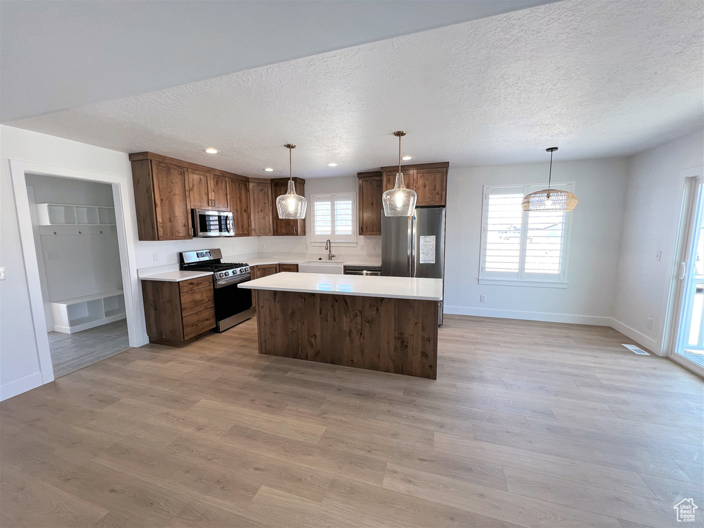 Kitchen featuring stainless steel appliances, a center island, a textured ceiling, light countertops, and light wood-style floors