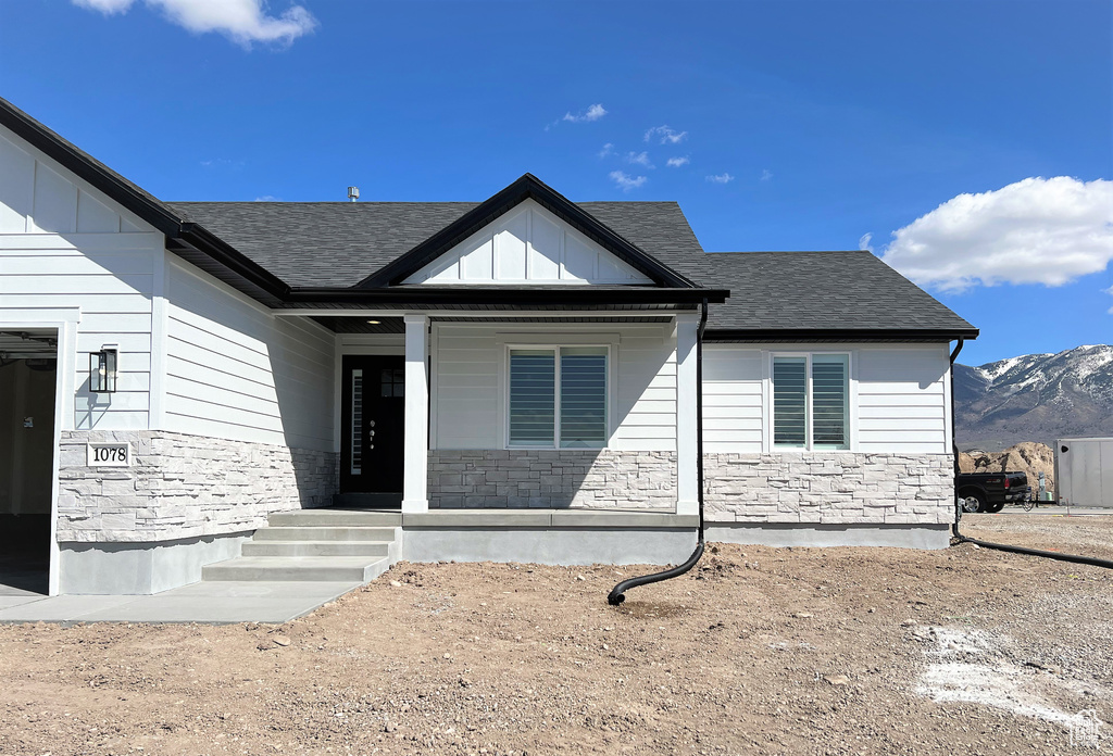 View of front of house with stone siding, covered porch, roof with shingles, and a mountain view