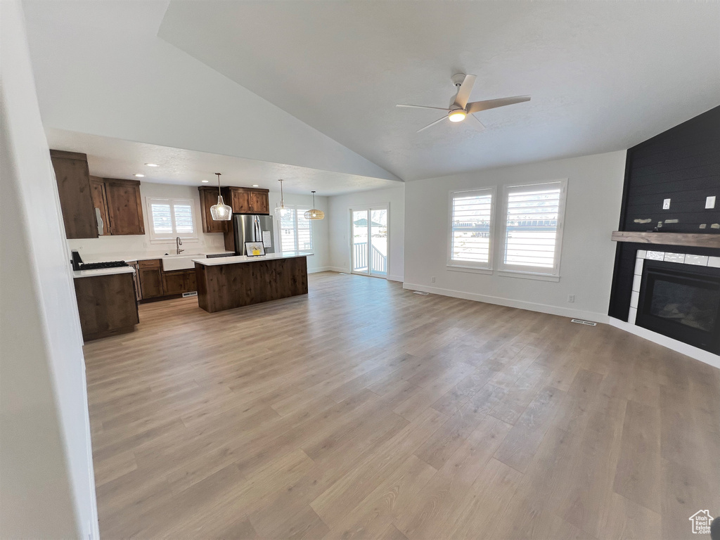 Unfurnished living room featuring a ceiling fan, plenty of natural light, a fireplace, light wood-type flooring, and high vaulted ceiling