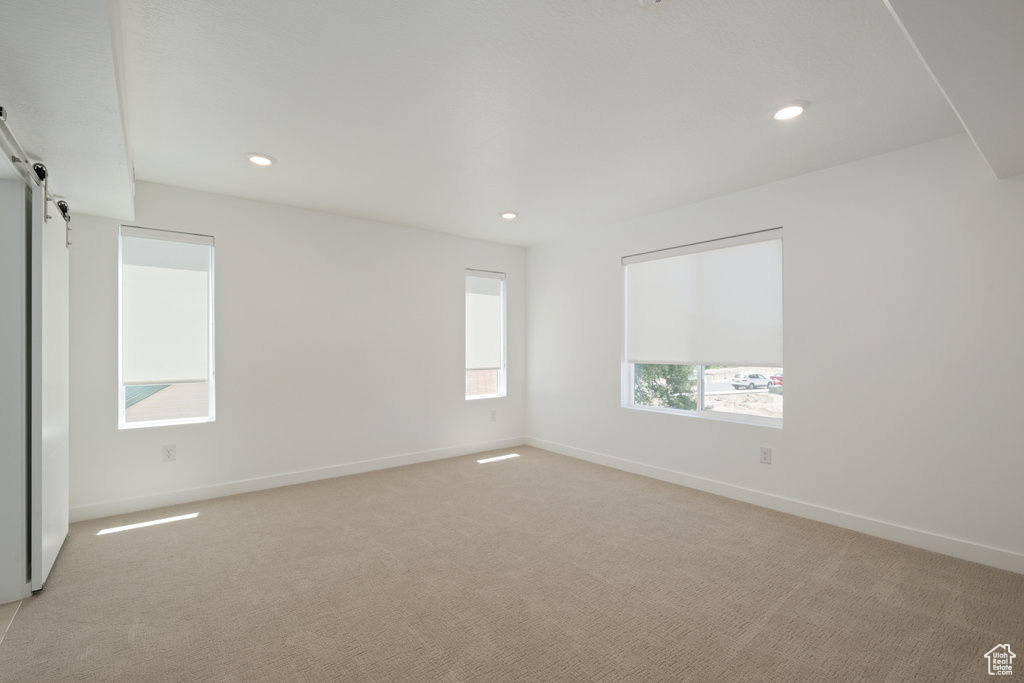 Empty room featuring light colored carpet, a barn door, and recessed lighting