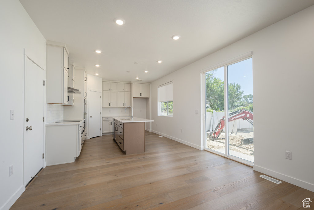 Kitchen with recessed lighting, light wood-style floors, white cabinetry, a kitchen island with sink, and light countertops