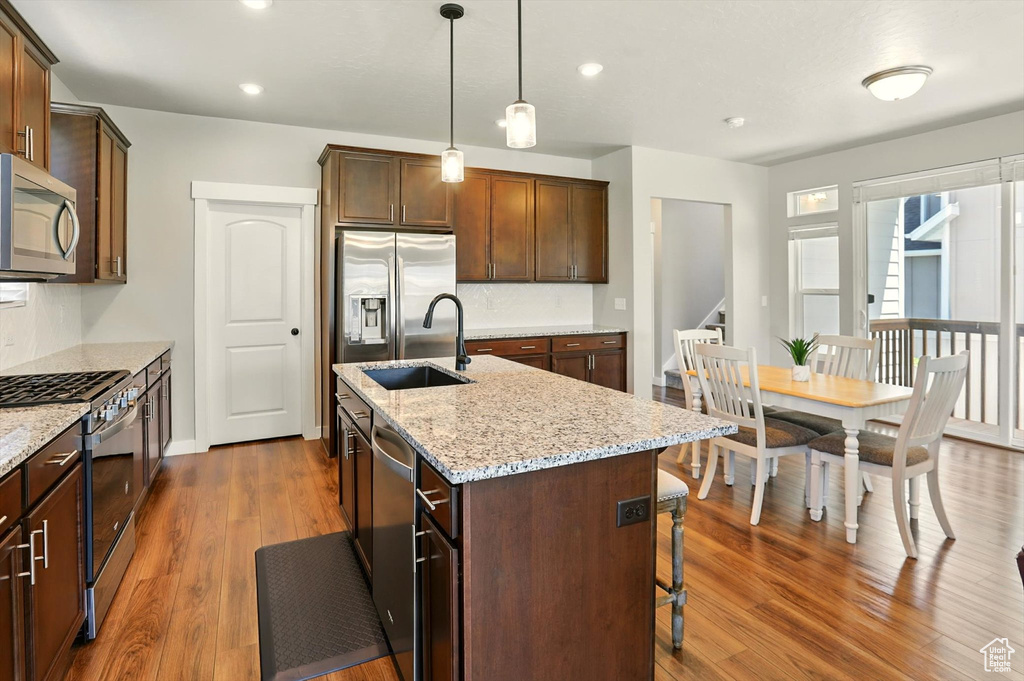 Kitchen with appliances with stainless steel finishes, dark wood-type flooring, a center island with sink, a kitchen bar, and light stone counters