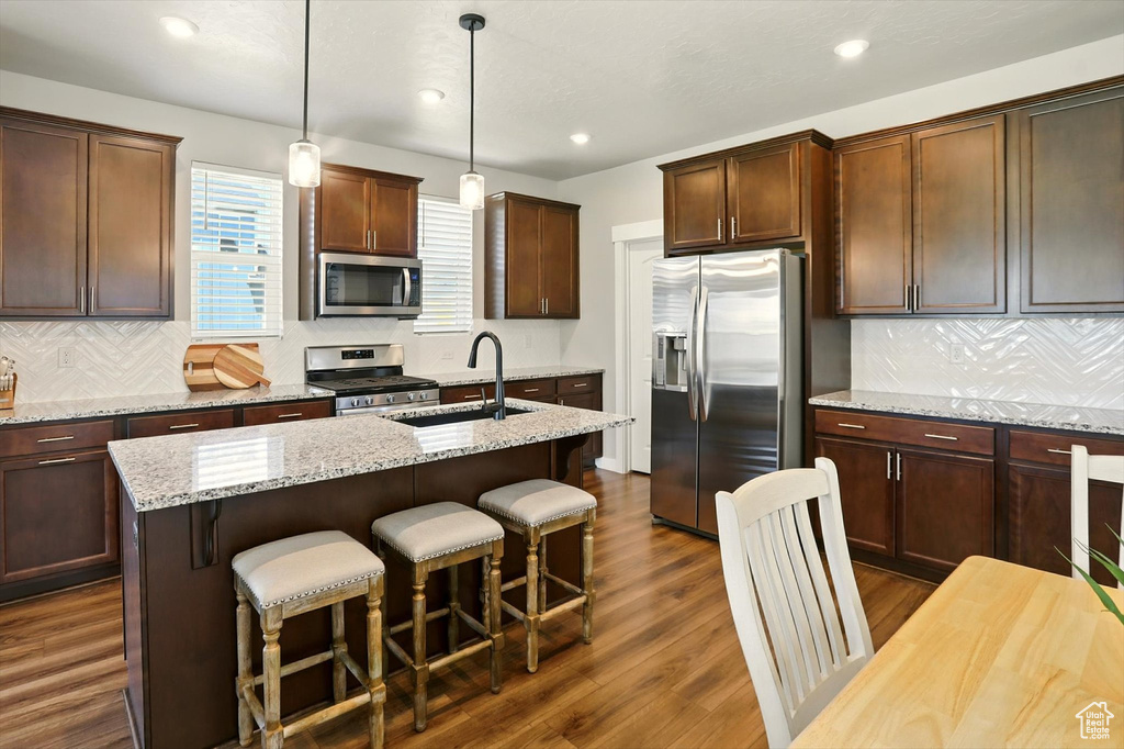 Kitchen featuring appliances with stainless steel finishes, a kitchen bar, a kitchen island with sink, backsplash, and recessed lighting