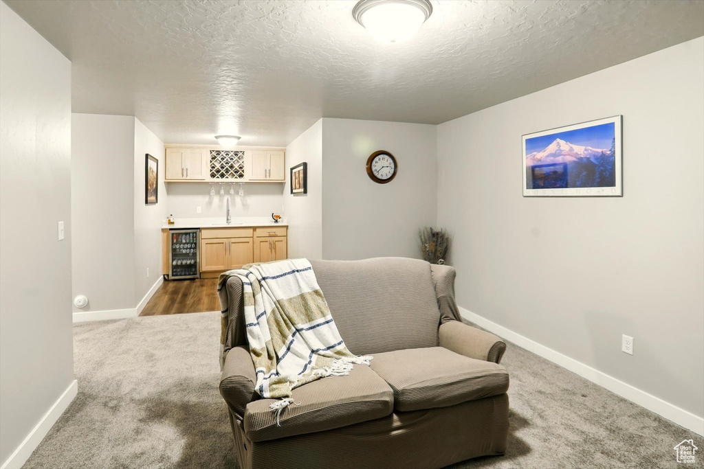 Living area featuring wine cooler, wet bar, carpet, and a textured ceiling