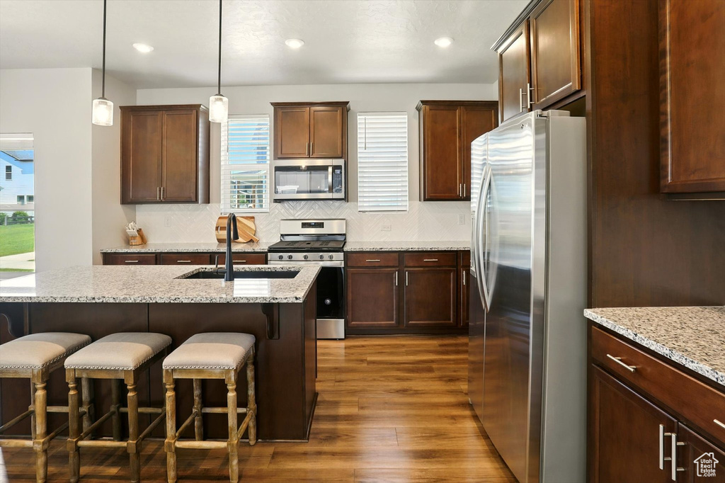 Kitchen featuring stainless steel appliances, dark wood-type flooring, a kitchen breakfast bar, decorative backsplash, and light stone counters
